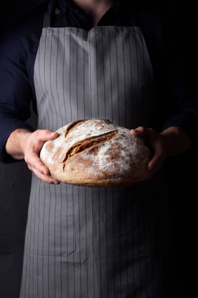 istock Baker holds bread in his hand on dark background 1209099031