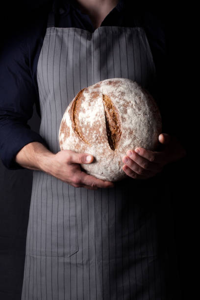 istock Baker holds bread in his hand on dark background 1209099036