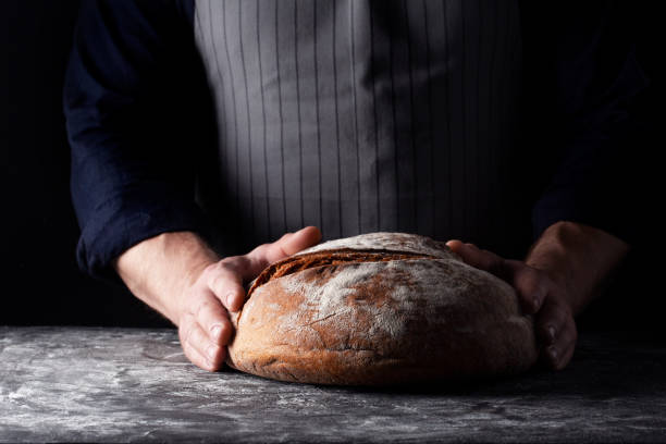 istock Baker holds bread in his hand on dark background 1209099116