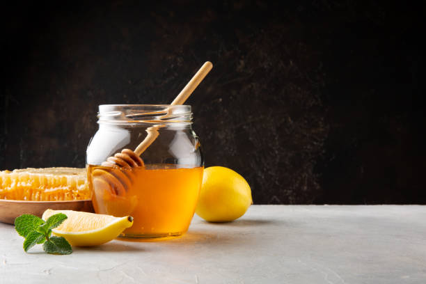 miel en un frasco de vidrio y panal, limón y menta sobre una mesa gris y fondo de pared oscuro - fruit winter orange lemon fotografías e imágenes de stock