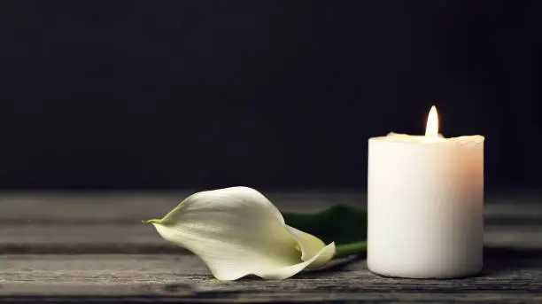 Photo of Burning candle and white calla on dark background with copy space. Sympathy card