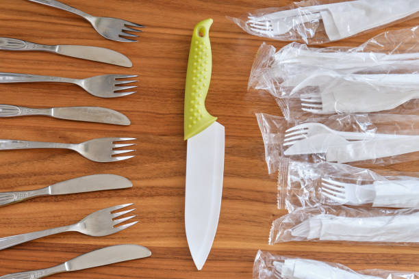 istock Big kitchen knife between disposable plastic sets and stainless steel fork & knife set, on a walnut table top. Concept for plastic cutlery versus reusable cutlery. 1209107610