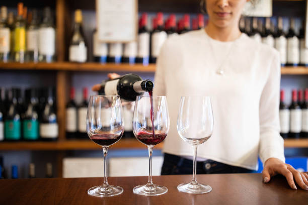 Bartender serving red wine in a winery Close-up of a female waiter pouring wine from bottle into three glasses on counter. Sommelier serving red wine in a winery store. winery stock pictures, royalty-free photos & images
