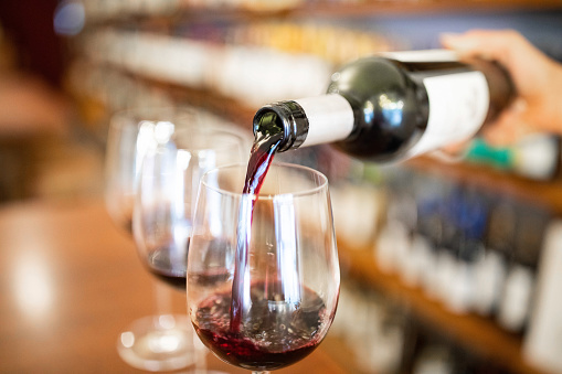 Close-up of a bartender hand pouring wine into glasses on bar counter. Waiter serving red wine in a cellar.