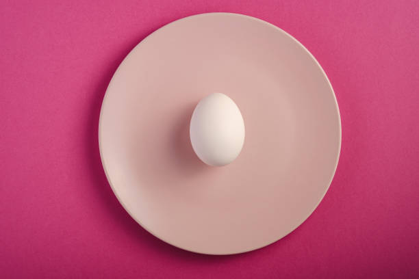 istock White egg in pink plate on purple plain minimal background, top view, happy Easter day 1209110494