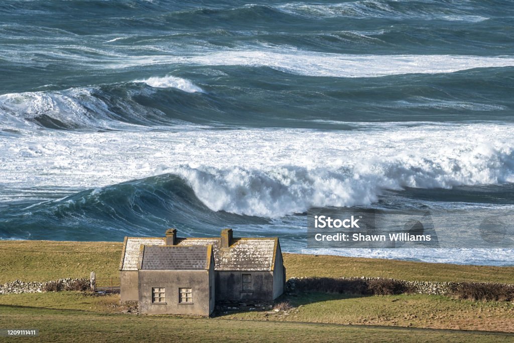 Rough Sea and a Lonely Cottage Rough sea with large waves on the Irish coastline in County Clare near the Cliffs of Moher Ireland Stock Photo