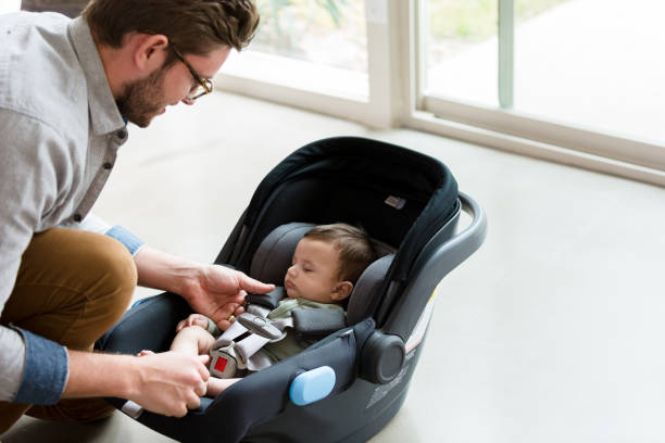New dad straps baby into infant car seat New dad makes sure his infant son is strapped in securly in an infant carrier. baby carrier stock pictures, royalty-free photos & images