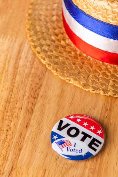 istock Looking down on a skimmer hat and a VOTE button with a “I VOTED” sticker sitting on a wood table 1209137039