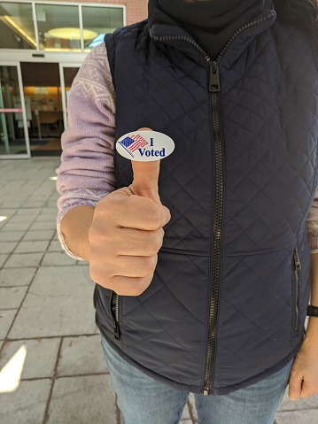 Voter holding up an I voted sticker on the thumb