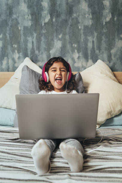 little girl with a computer laughing on the bed - child computer laptop little girls imagens e fotografias de stock