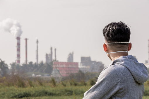 back view of asian man look something and wears protective n95 mask against air pollution in front of factoryasian man look to you and wears protective n95 mask against air pollution standing in front of factory