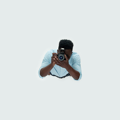 Aerial view of aged 20-29 years old with short hair caucasian male photographer standing in front of white background who is excited who is photographing and holding camera