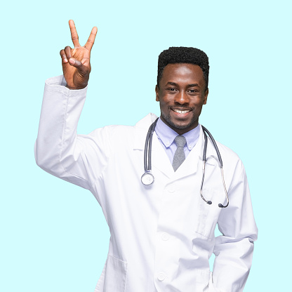 One person of with short hair african ethnicity young male doctor standing in front of blue background wearing lab coat who is successful and showing two fingers