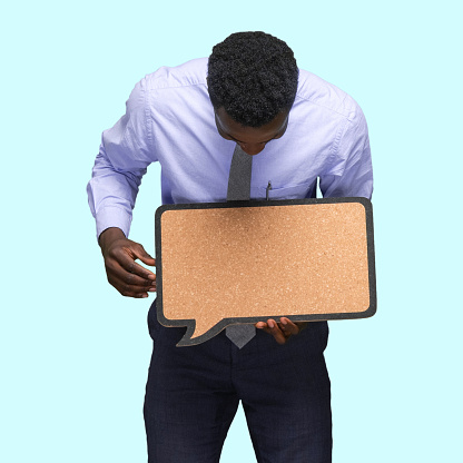 Waist up of african-american ethnicity young male business person standing in front of colored background who is contemplating who is showing with hand and holding questionnaire with copy space