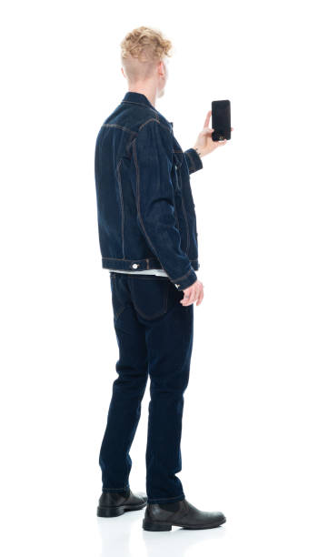 Caucasian young male photography standing in front of white background wearing shirt and using smart phone Rear view of aged 20-29 years old with blond hair caucasian young male photography standing in front of white background wearing shirt who is showing cool attitude who is taking a selfie and using smart phone human back photos stock pictures, royalty-free photos & images