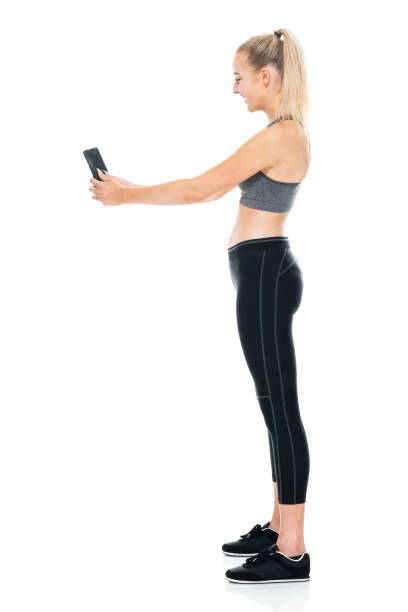 istock Generation z female standing in front of white background wearing spandex and using mobile phone 1209153949