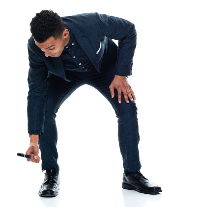 Full length of aged 20-29 years old with black hair african-american ethnicity young male detective crouching in front of white background wearing smart casual who is curious who is examining and holding magnifying glass