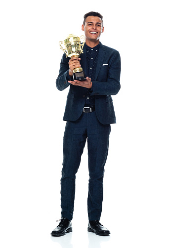 Full length of aged 20-29 years old with black hair african-american ethnicity young male business person standing in front of white background wearing business casual who is successful and winning and showing award who is in first place and holding trophy