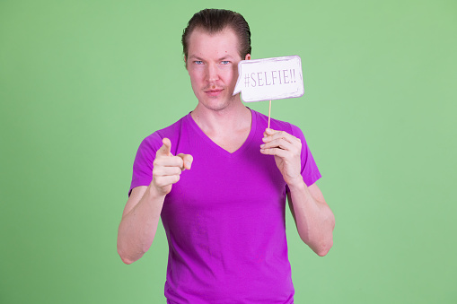 Studio shot of young handsome Scandinavian man wearing purple shirt against green background