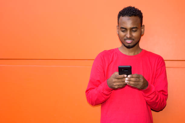 istock Happy young African bearded man using phone against orange wall 1209159315