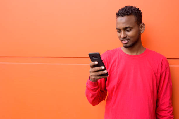 istock Happy young African bearded man with Afro hair using phone against orange wall 1209159321