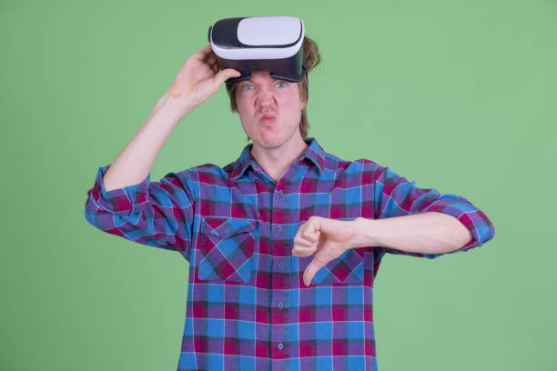 istock Stressed young hipster man removing virtual reality headset and giving thumbs down 1209159516