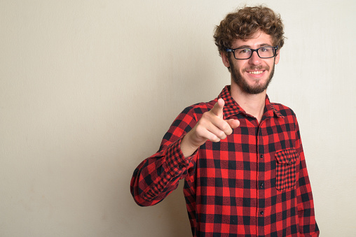 Studio shot of young handsome bearded hipster man with curly hair wearing eyeglasses against white background