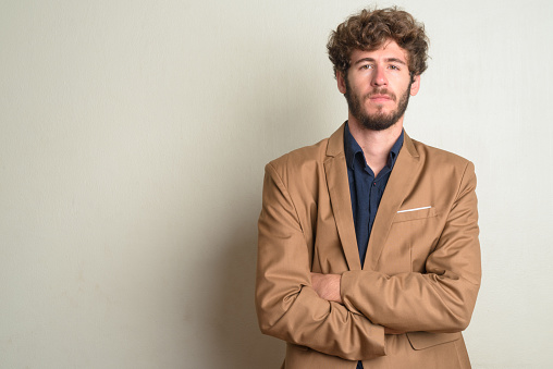 Studio shot of young handsome bearded businessman with curly hair wearing suit against white background