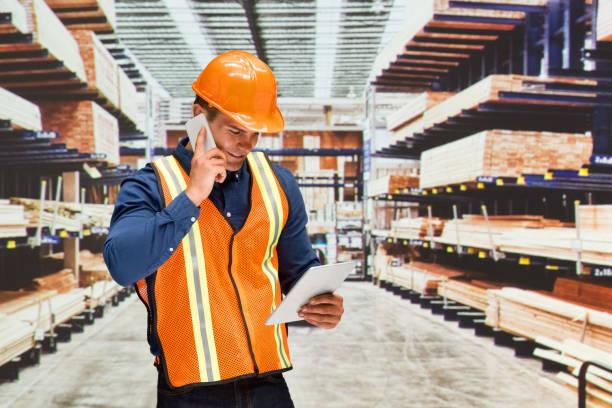 young male construction worker standing at the storage room in front of merchandise in the store wearing helmet and using digital tablet - building contractor engineer digital tablet construction imagens e fotografias de stock