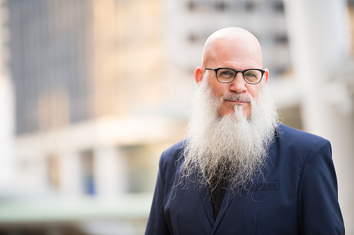 Portrait of mature bald businessman with long beard wearing eyeglasses in the city streets outdoors