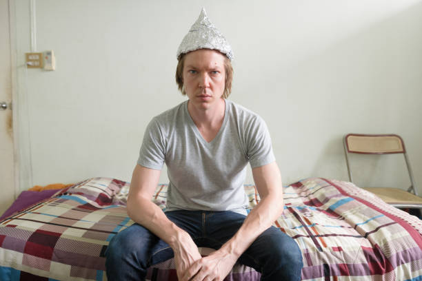 Young man with tin foil hat in the bedroom Portrait of young handsome man wearing tin foil hat as conspiracy theory concept in the bedroom at home tin foil hat stock pictures, royalty-free photos & images