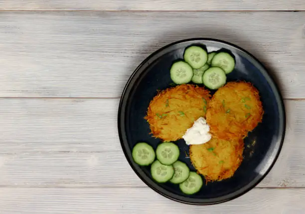 Hashbrowns on a plate on a light wooden background. Served with sour cream. Top view, flat lay.