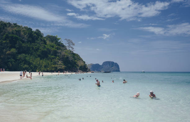 Aerial summer view of a secluded white sand beach in Phuket, Thailand. People are walking along the beach, swimming in the turquoise water or laying down resting on the white sand beach.
