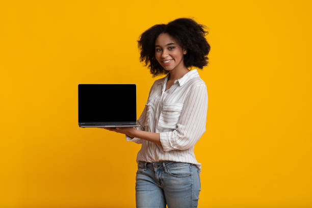 istock Beautiful Afro Woman Demonstrating Laptop Computer With Black Blank Screen 1209184729
