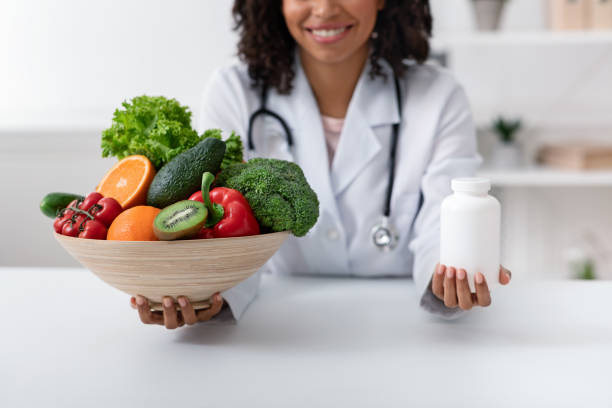 栄養士は、果物、野菜、丸薬のボトルとボウルを保持しています - nutritional supplement pill eating food ストックフォトと画像