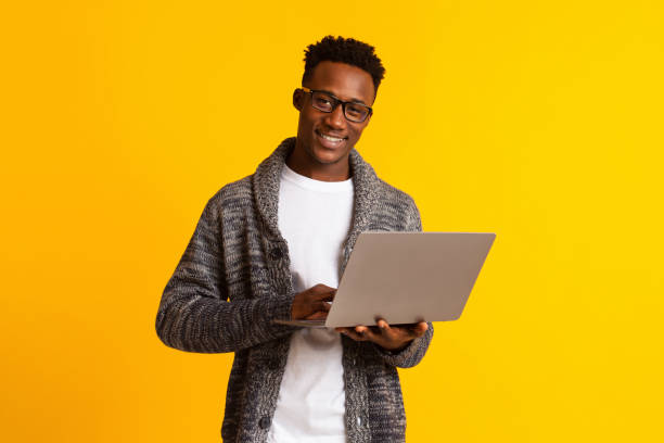 istock Handsome young african man using laptop on yellow 1209187517