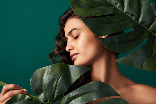 Cropped shot of a beautiful young woman posing with monstera leaves against a green background
