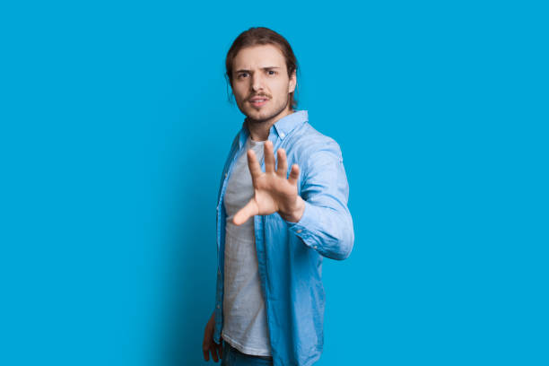 istock Caucasian man looking at camera and gesturing like he wants to stop something while posing on a blue wall 1209191259