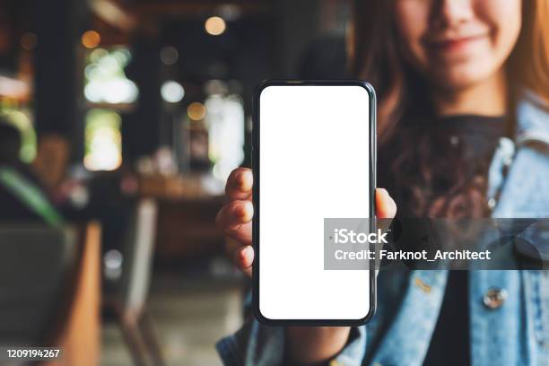 A Woman Holding And Showing Black Mobile Phone With Blank White Screen In Cafe Stock Photo - Download Image Now