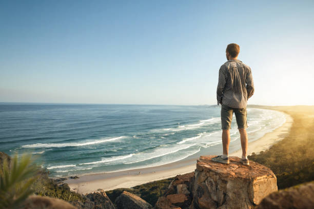 man high above a beautiful coastline at dusk - men beach back rear view imagens e fotografias de stock