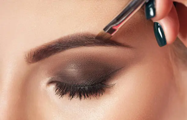 Photo of Make-up artist does eyebrow make-up to a woman with smoky eyes makeup. Beautiful thick eyebrows close up. Professional makeup and cosmetology skin care.