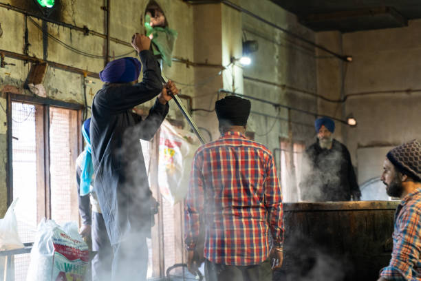 A Sikh man stirs a steaming pot of food in the kitchen (langer) at the Golden Temple stock photo