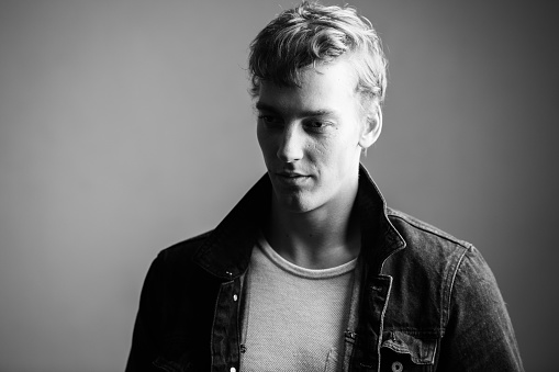 Studio shot of young handsome Scandinavian man with curly hair against white background in black and white