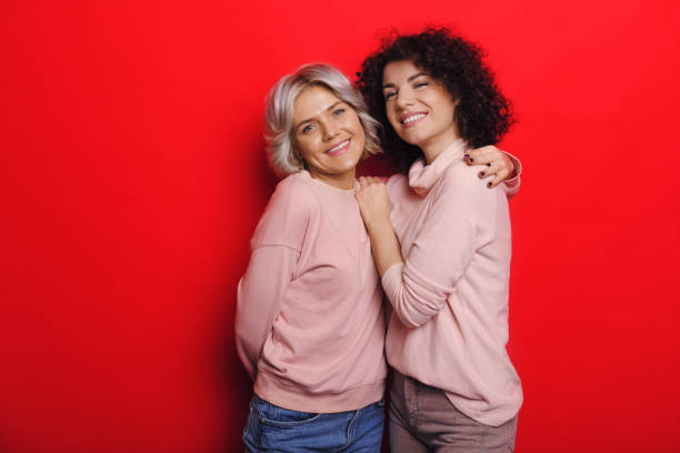 istock Curly haired lady with her blonde friend embracing cheerfully on a red background 1209201817