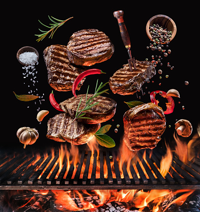 Grilled beef steaks and vegetables in motion falling down on open grill.  Conceptual photo of meat or barbeque cooking process.