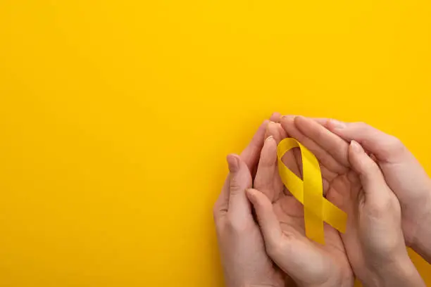 Photo of Cropped view of woman and man holding yellow ribbon on colorful background, international childhood cancer day concept