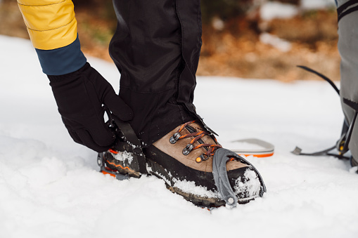 Adult man putting crampons on his winter shoes, getting ready for a hike in the winter mountains.