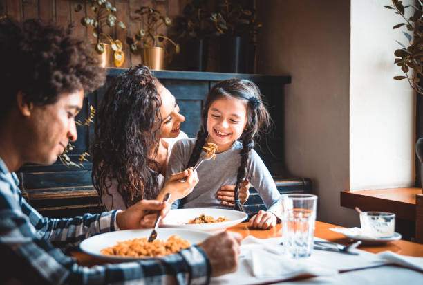 felice famiglia afro-americana mangiare il pranzo insieme al ristorante e divertirsi - child caribbean black latin american and hispanic ethnicity foto e immagini stock