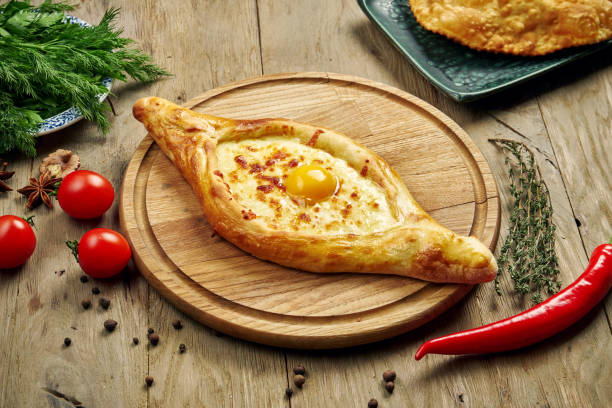 Top view on tasty traditional Adjarian Khachapuri - open baked pie with melted salt cheese (suluguni) and egg yolk on wooden tray. Traditional georgian food stock photo