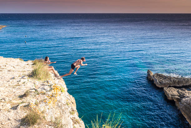 istock Man Jumping From Cliff Into Sea On Sunny Day 1209239368